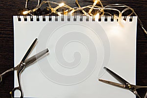 Hairdresser tools on dark wooden background. Blank paper notepad with barber accessories flat lay.