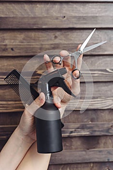 Hairdresser tools on a wooden background in the hands of a master. Dark tint. Protective spray, comb and hair scissors