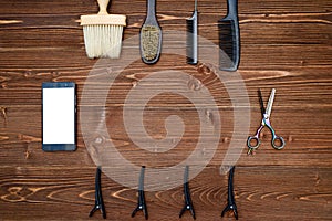 Hairdresser tools on wooden background. Top view on wooden table with scissors, comb, brush and hairclips with phone, free space.