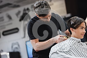 Hairdresser trimming hair of teenage boy