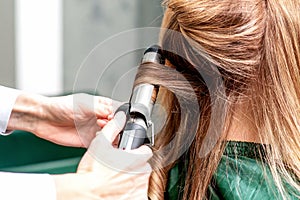 Hairdresser uses curling iron for twists hair of woman