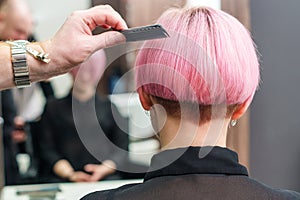 The hairdresser is using comb for female pink hair at beauty salon