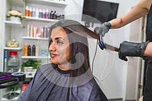 Hairdresser using a hair straightened to straighten the hair. Hair stylist working on a woman`s hair style at salon