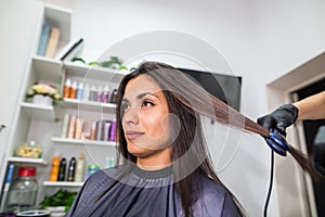 Hairdresser using a hair straightened to straighten the hair. Hair stylist working on a woman`s hair style at salon