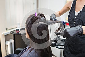Hairdresser using a hair straightened to straighten the hair. Hair stylist working on a woman`s hair style at salon