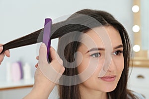 Hairdresser using modern flat iron to style client`s hair