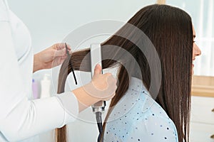 Hairdresser using modern flat iron to style client`s hair