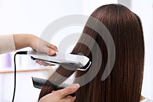 Hairdresser using modern flat iron to style client`s hair