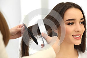 Hairdresser using modern flat iron to style client`s hair