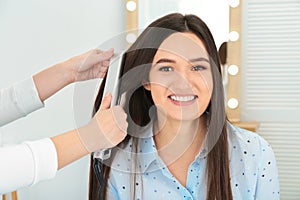 Hairdresser using modern flat iron to style client`s hair