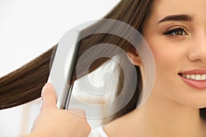 Hairdresser using modern flat iron to style client`s hair in salon