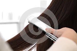 Hairdresser using modern flat iron to style client`s hair in salon