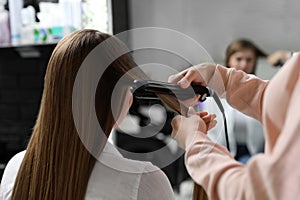 Hairdresser using straightener to style client`s hair