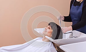 The hairdresser washes the shampoo off the hair to a young girl, brunette