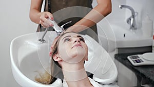 Hairdresser washing girl's head in white sink in salon