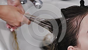 Hairdresser washing woman`s hair with shampoo in white sink