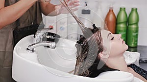 Hairdresser washing woman's hair with shampoo in white sink