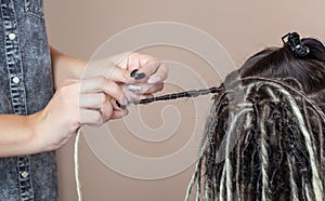 A hairdresser weaves dreadlocks to a beautiful young girl in a hairdresser`s. Professional hair care and creating hairstyles