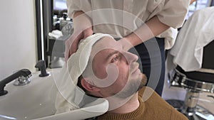 A hairdresser wipes a client man head with a white towel after washing in a barbershop.