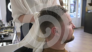 A hairdresser wipes a client man head with a white towel after washing in a barbershop.