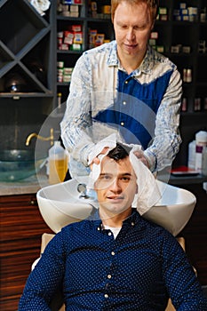 hairdresser wipes hair of brunette man with disposable towel after washing hair