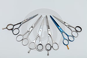 Hairdressing equipment like different scissors on gray wooden table in professional salon with copy place