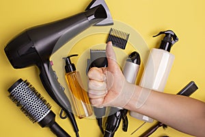 Hairdressing tools in black: hair dryer, combs, sprays, clipper and female hand with thumbs up on a yellow background, flat lay
