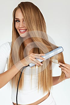 Hairdressing. Woman With Beautiful Long Hair Using Straightener