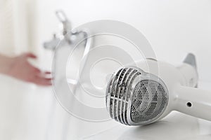 Hairdryer lying on a bathtub with hand and flowing water from a faucet in the background