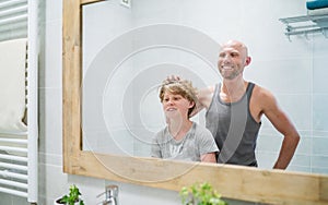 Hairless dad and his long-haired teen son in bathroom in front of the mirror. Father rising up kid`s hairs thinking about his new