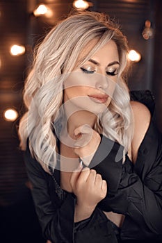 Hairstyle. Beautiful blonde woman portrait posing in black shirt. Fashionable blond girl model over bokeh lights dark background