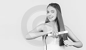 Hairstyle. Beautiful smiling woman ironing long hair with flat iron. Portrait of young beautiful girl using styler on