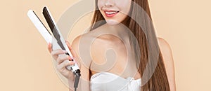 Hairstyle. Beautiful smiling woman ironing long hair with flat iron. Woman straightening hair with straightener