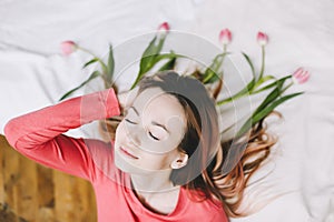 Hairstyle with flowers. Romantic portrait of a girl in bed with natural flowers. Young woman with tulips in hair. Beautiful photo