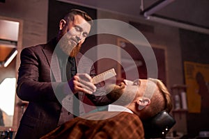 Hairstyling process. barber cutting beard of caucasian male