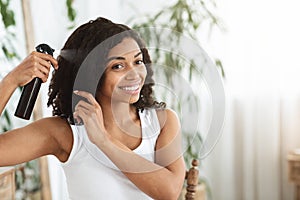 Hairstyling. Smiling Black Woman Applying Texturising Spray To Her Beautiful Curly Hair