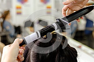 Hairstylist curling hair close up. Hairdresser making hairstyle to brown long hair woman in beauty salon. Professional hair care,