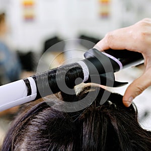 Hairstylist curling hair close up. Hairdresser making hairstyle to brown long hair woman in beauty salon. Professional hair care,