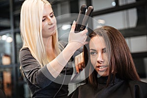 Hairstylist curling hair woman client in hairdressing beauty salon