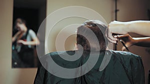 Hairstylist cut boy hair during haircutting in hairdressing salon.