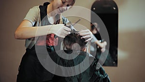 Hairstylist cut boy hair during haircutting in hairdressing salon.