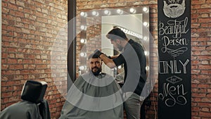 Hairstylist cutting hair to handsome client in barbershop