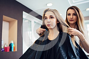 Hairstylist deciding with the young female customer what haircut to do in hairdressing parlor. Two pretty blondes