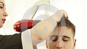 Hairstylist drying male hair after hairdressing in barber shop. Close up barber styling hair with dryer after washing