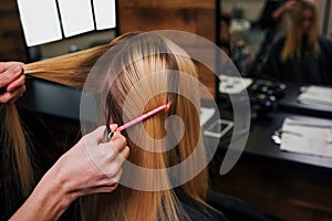 Hairstylist hands holding strand of blonde hair while combing it before haircut in salon