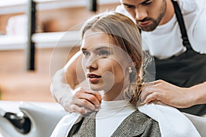 Hairstylist putting towel on client shoulders and young woman looking away