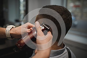 Hairstylist serving client at a barbershop. Rear view shot of hairdresser`s hands shaving male client`s head. Beauty