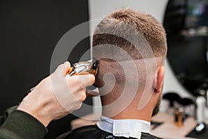 Hairstylist shaves male occiput with trimmer in barbershop