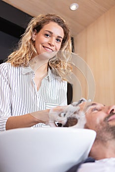 hairstylist smiling at camera while washing clients hair