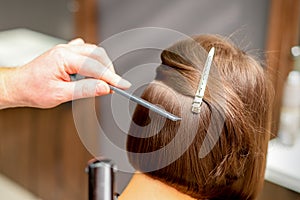 Hairstylist is straightening short hair of young brunette woman with a flat iron in a hairdresser salon, close up.